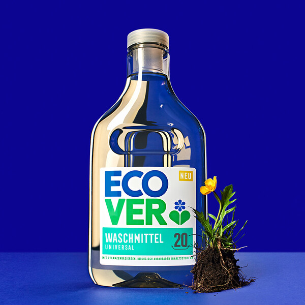 Ecover Keyvisual Ecover Waschmittelflasche mit kleiner Butterblume und Wurzeln auf blauem Hintergrund