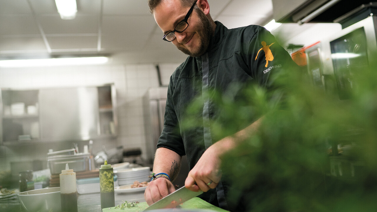 StrandGut Resorts lachender Koch schneidet Gem&uuml;se in der Kueche