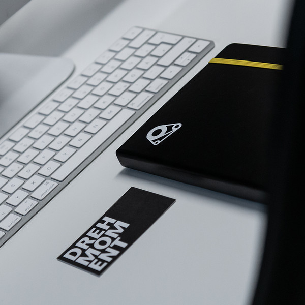 Schreibtisch mit silbernem Apple iMac, Notizbuch und Visitenkarte mit DREHMOMENT Logo