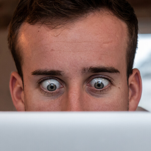 Mann schaut mit weit geoeffneten Augen auf ein Laptop Bildschirm